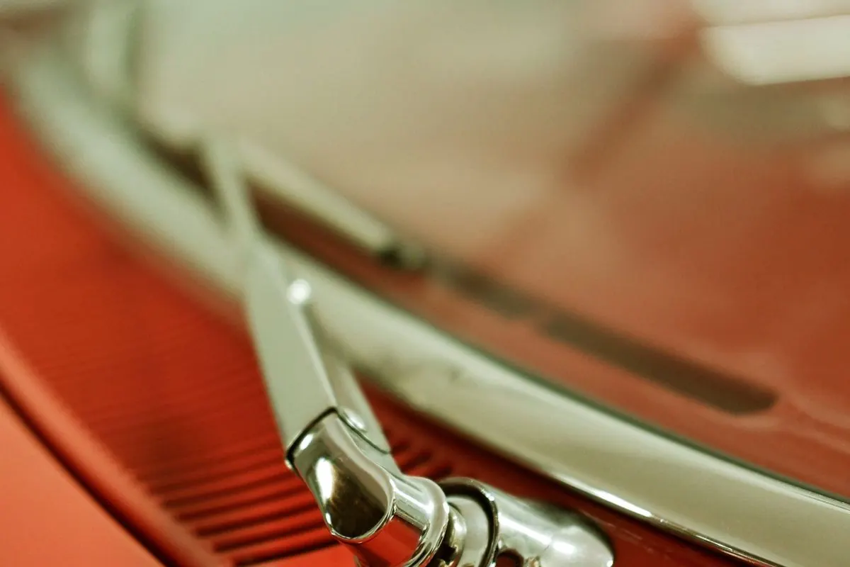 Chrome windscreen wiper arm mounted on a red car bonnet