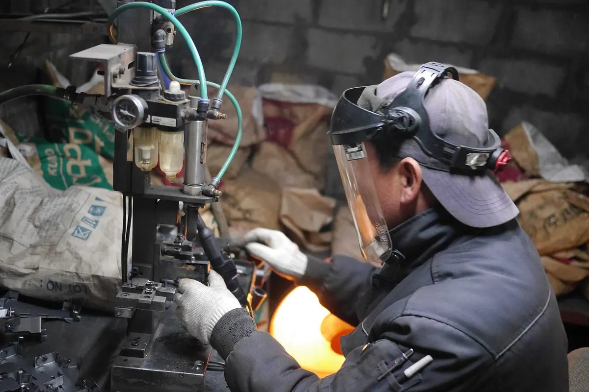 Worker in a face shield operating a spot welding machine