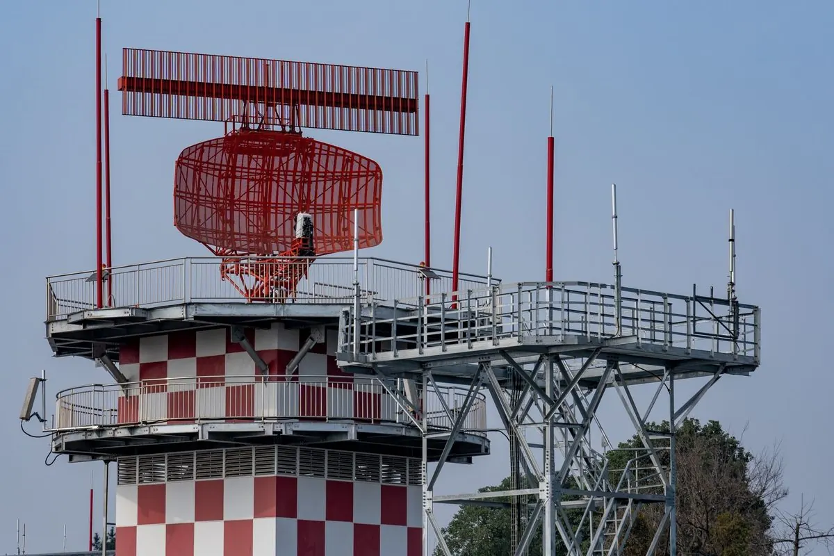 Red and white airport radar tower under a blue sky