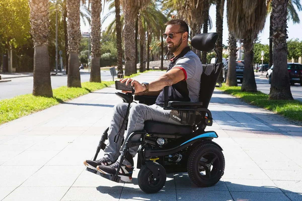 Man riding a powered wheelchair along a pavement