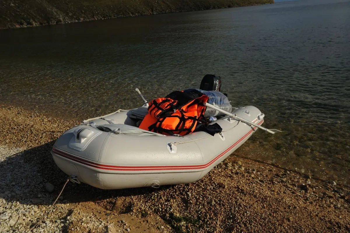 Gray inflatable boat with outboard motor on a gravel shore