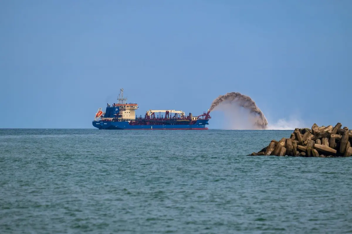 Dredger ship spraying sand near a breakwater