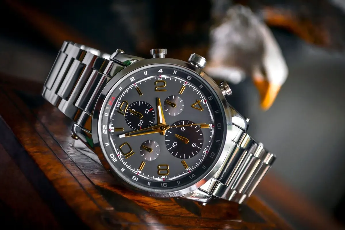 Đồng hồ đeo tay chronograph dây thép bạc đặt trên mặt bàn gỗ