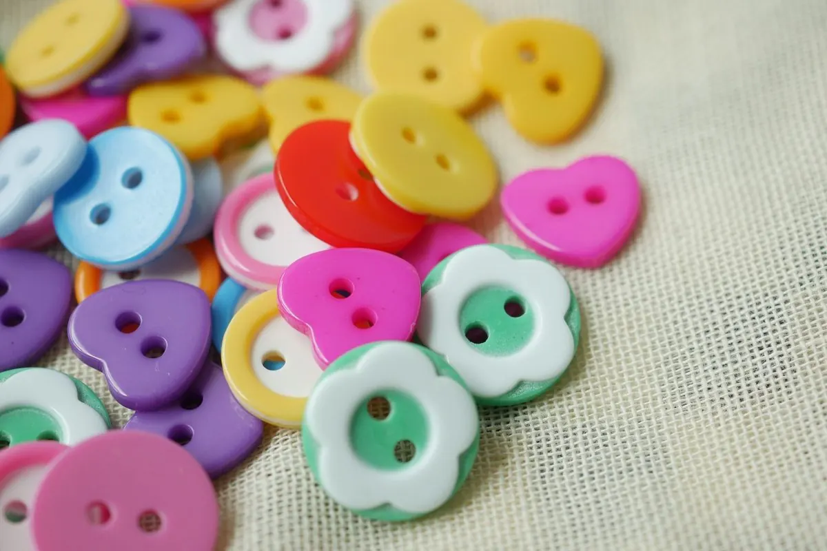 Colourful plastic sewing buttons of various shapes on fabric