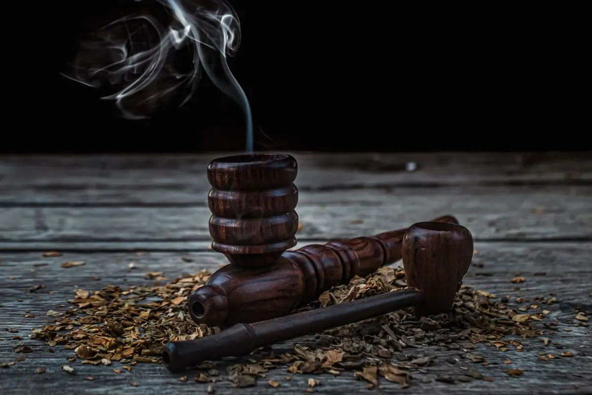 Wooden smoking pipe lying on loose tobacco with rising smoke