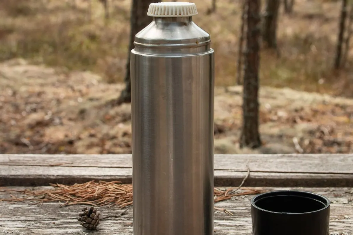 Bình giữ nhiệt inox đặt trên bàn gỗ trong rừng thông