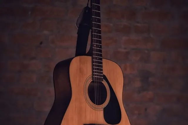 Cây đàn guitar gỗ dựa vào tường gạch nâu